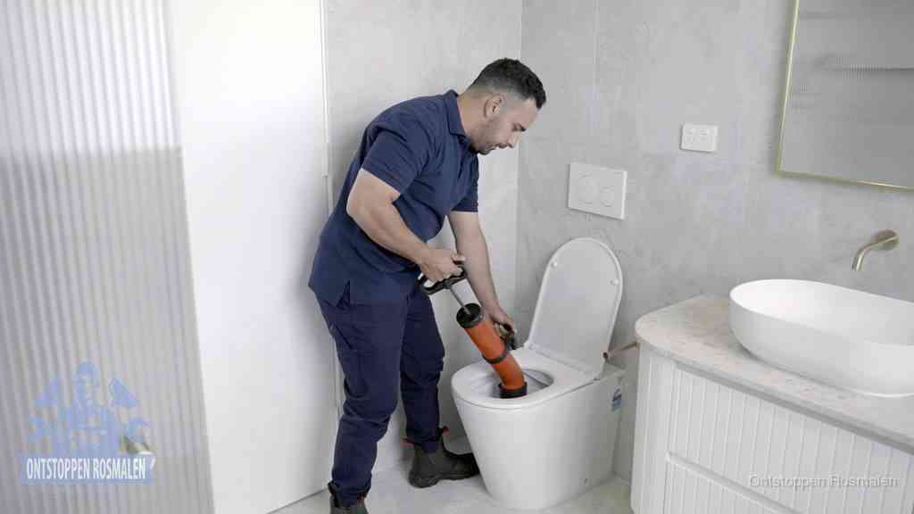Een monteur buigt over een wandcloset en duwt met de hand een persluchtontstopper in de toiletpot om de verstopping handmatig los te maken in Rosmalen