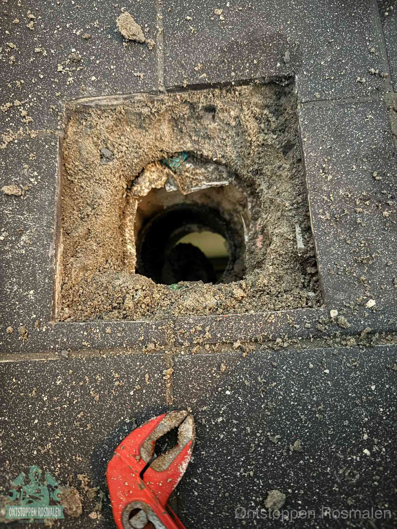 Een geopend rioolputje in een betontegelvloer met losgemaakt rooster en een zichtbare ronde afvoerbuis, het achterhalen waar de afvoerverstopping zit in Rosmalen