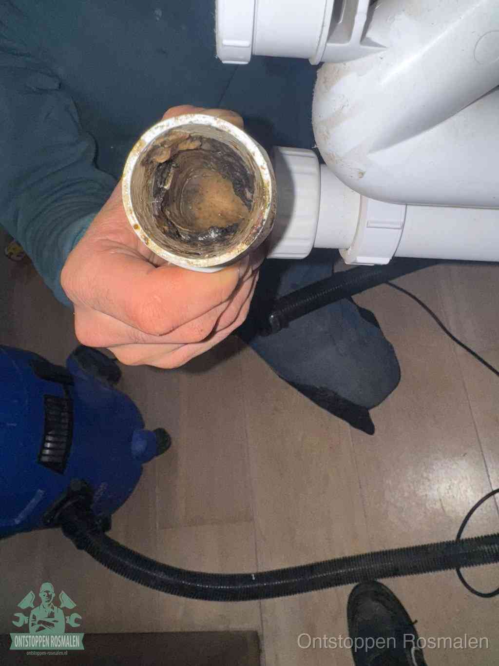Een hand houdt een losgekoppeld PVC-afvoerbuisstuk vast dat van binnen volledig is dichtgeslibd met vet, vuil en aanslag, de meest voorkomende oorzaak van een verstopte afvoer in Rosmalen