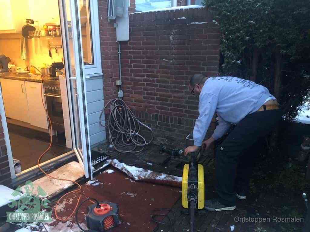 Een monteur werkt buiten bij een open riool-/grondput met een elektrische ontstoppingsmachine om een verborgen afvoerprobleem op te sporen in Rosmalen