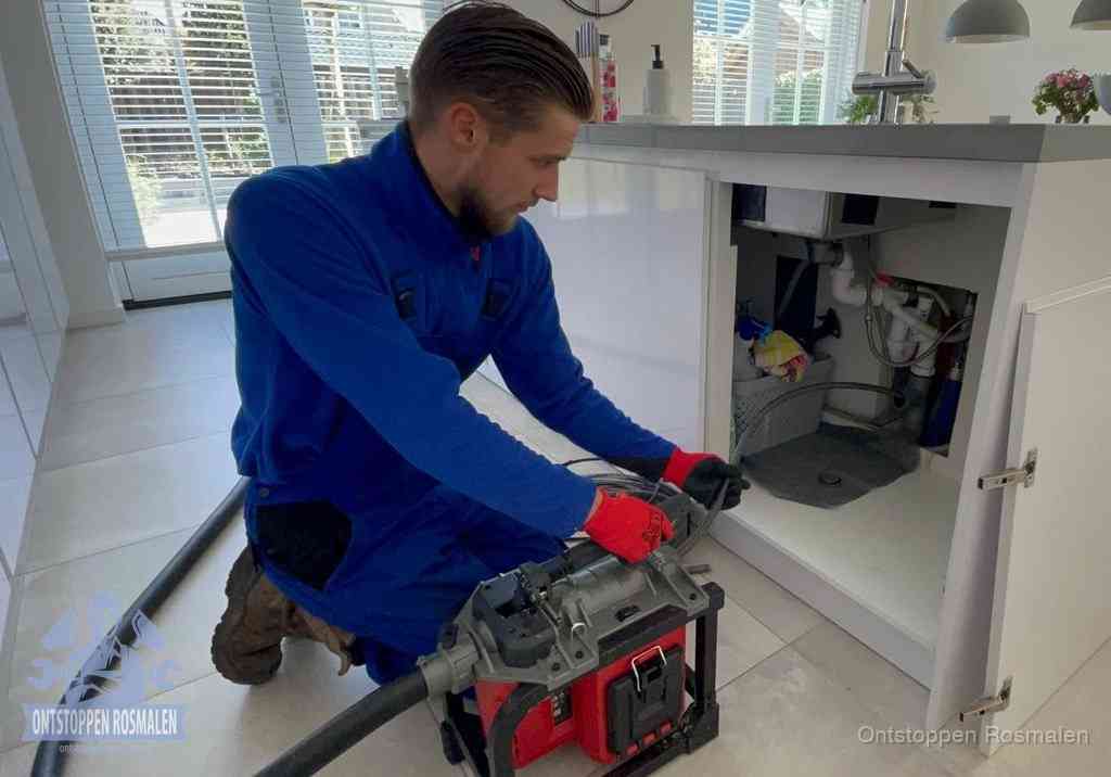 Een monteur voert een professionele elektrische ontstoppingsmachine in de afvoer onder de spoelbak tijdens het gootsteen ontstoppen in Rosmalen