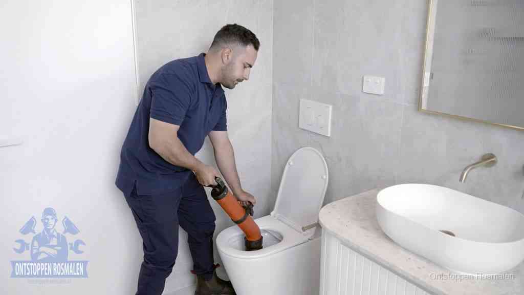 Een man gebruikt een handmatige luchtdruk-ontstopper in een modern betegeld toilet om zelf de wc te ontstoppen in Rosmalen